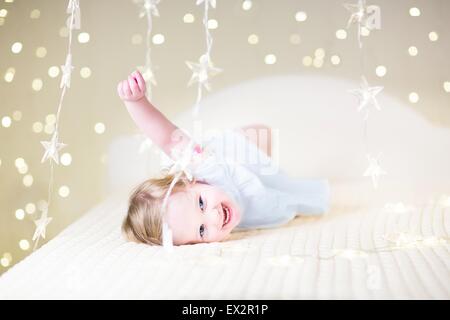 Carino il toddler ragazza che gioca su un letto tra caldo morbido luci di Natale Foto Stock