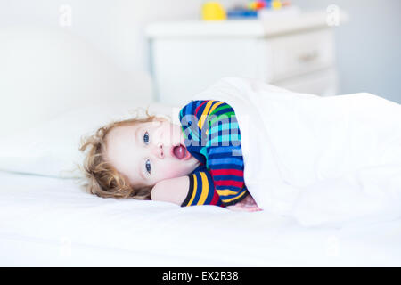 Funny sbadigli toddler girl svegliarsi al mattino in una soleggiata camera bianca Foto Stock