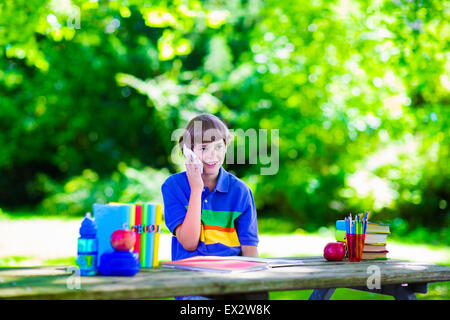 Bambino a scuola con telefono. Smart ragazzo adolescente studiare e imparare in esterni, la lettura di libri. Bambini chiamando, Foto Stock