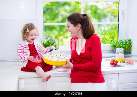 La madre e il bambino cuocere una torta. Giovane donna e sua figlia di cucinare in una cucina bianca. Bambini pasticceria da forno. Foto Stock