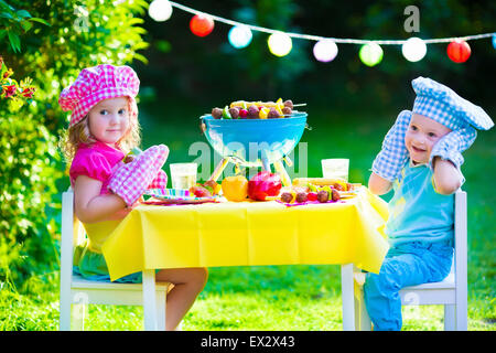 Bambini cuocere carne. Camping Famiglia e godendo di barbecue. Fratello e Sorella a barbecue la preparazione di bistecche e salsicce. Foto Stock