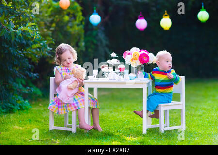 Giardino festa di compleanno per bambini. Bambini celebrazione all'aperto. Piccolo Ragazzo e ragazza bere il tè e mangiare la torta nel cortile posteriore Foto Stock