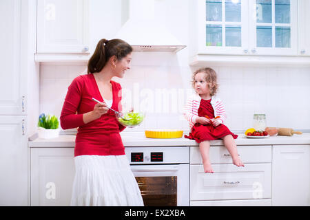 La madre e il bambino cuocere una torta. Giovane donna e sua figlia di cucinare in una cucina bianca. Bambini pasticceria da forno. Foto Stock