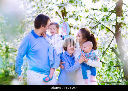 Famiglia con bambini in una molla in fiore giardino. I genitori con tre bambini - baby, bimbo piccolo ragazzo e una ragazza godendo picnic su un maso Foto Stock