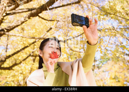 Senior donna giapponese prendendo un selfie in un parco della città in autunno Foto Stock