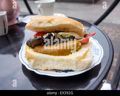 La colazione panino con pancetta salsiccia funghi uovo fritto prugna pomodoro e una tazza di tè Foto Stock