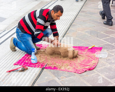 L'artista di strada in un centro commerciale con la sua scultura di sabbia di un cane Foto Stock