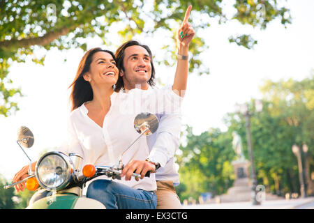 Sorridente coppia giovane su scooter insieme mentre la donna puntare il dito lontano dalla città Foto Stock