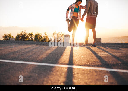 Colpo all'aperto di giovani praticanti di jogging stretching prima di una corsa la mattina. Giovane uomo e donna stretching le gambe a sunrise. Foto Stock