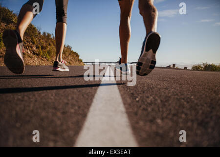 Ritagliato shot di corridori di marcia su strada. Vista posteriore di close-up immagine di uomo e donna jogging all'aperto. Concentrarsi sulla strada e gambe Foto Stock