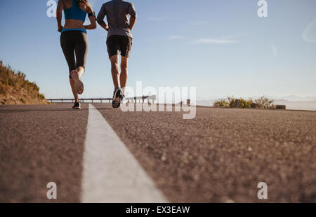 Vista posteriore mozzato colpo di due giovani in esecuzione insieme sulla strada. L uomo e la donna sulla corsa mattutina sul giorno di estate. Bassa angolazione Foto Stock