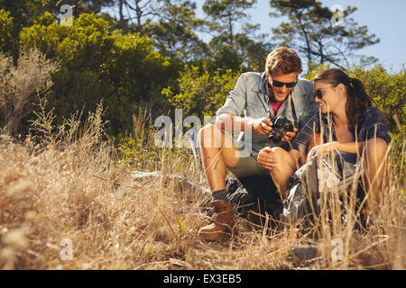 Coppia giovane all'esterno guardando le foto sulla fotocamera. Uomo caucasico e donna su escursioni di viaggio prendendo una pausa. Foto Stock