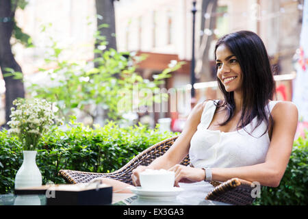 Felice giovane donna seduta nella caffetteria all'aperto con tazza di caffè Foto Stock