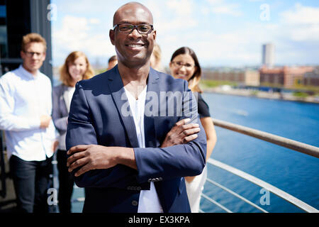 Maschio nero executive in piedi con le braccia incrociate di fronte ai colleghi Foto Stock
