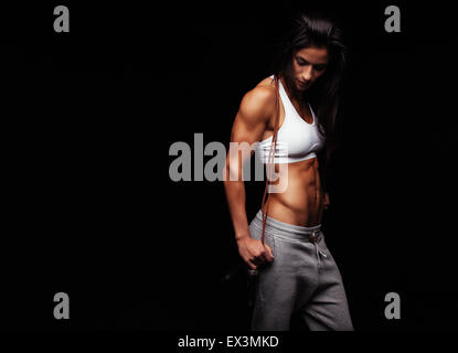 Colpo di giovani femmine esercizi con un salto con la corda guardando verso il basso. Donna muscolare con funi di salto su sfondo nero, copys Foto Stock