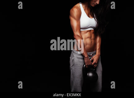 Ritagliato colpo di atleta femminile facendo body building esercizio con bollitore bell su sfondo nero. Foto Stock