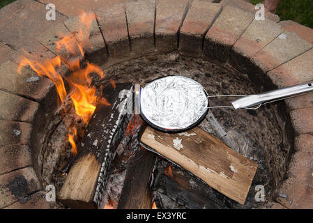 La cottura di una padella di popcorn in una lamina coperto recipiente al di sopra di un giardino una buca per il fuoco. Foto Stock