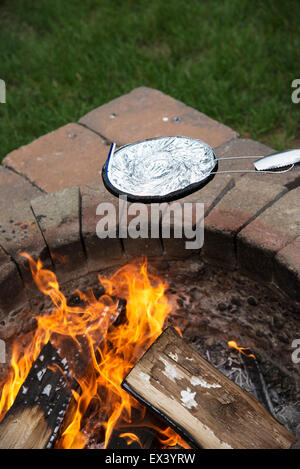 La cottura di una padella di popcorn in una lamina coperto recipiente al di sopra di un giardino una buca per il fuoco. Foto Stock