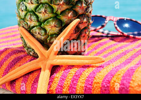 Primo piano di una stella di mare, un ananas e un paio di occhiali da sole in un colorato telo da spiaggia Foto Stock