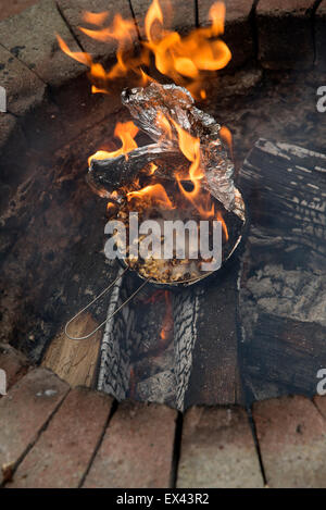 Il Popcorn in una lamina tegame coperto esplode e prende fuoco in un giardino una buca per il fuoco le fiamme con la masterizzazione ora popcorn immangiabile Foto Stock