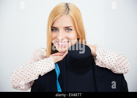 Donna sorridente designer appoggiata sul manichino e guardando la telecamera su uno sfondo grigio Foto Stock