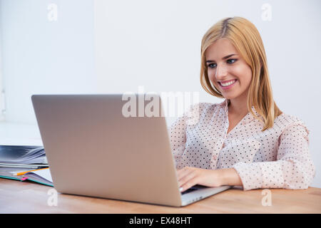 Sorridente giovane imprenditrice seduti a tavola e utilizzo di notebook in ufficio Foto Stock