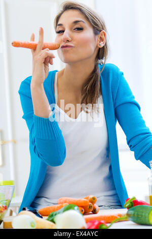 Ritratto di bella donna giovane avendo divertimento con una carota in cucina Foto Stock