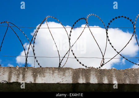 Filo spinato sulla sommità della recinzione in cemento armato con cielo blu con nuvole closeup Foto Stock