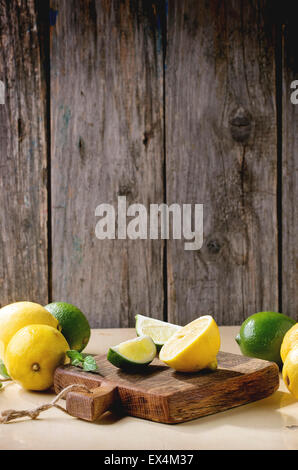 Cumulo di tutto e fette di limoni e limette sul piccolo tagliere di legno su sfondo di legno. Rustico luce sun. Foto Stock