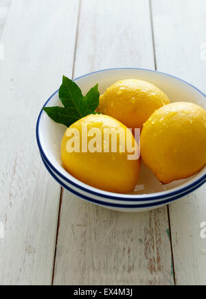 Tre limoni in una ciotola su un bianco sullo sfondo di legno Foto Stock