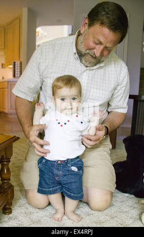 7 mese vecchia ragazza molto orgoglioso di se stessa per piedi mentre è appesa sul suo nonno Foto Stock