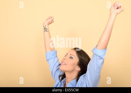 Attraente giovane donna seduta sul pavimento che indossa una maglietta blu e bianco jeans alzando le mani in eccitazione Foto Stock