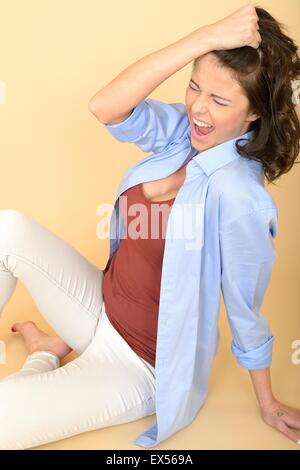 Attraente stressato e frustrato donna seduta sul pavimento che indossa una maglietta blu e bianco jeans tirando i suoi capelli in rabbia Foto Stock