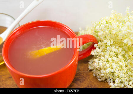 Anziano sano tè con limone servita con una ciotola di miele con un bilanciere su una tavola decorata con elderflowers Foto Stock