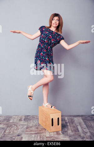 A piena lunghezza Ritratto di una donna divertente stare in piedi su una gamba sola su una scatola di legno Foto Stock