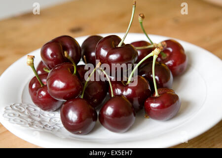 Ciliegie rosse fresche disposte su un piatto bianco, fotografate dall'alto. Una composizione di frutta estiva semplice e vibrante su uno sfondo pulito. Foto Stock