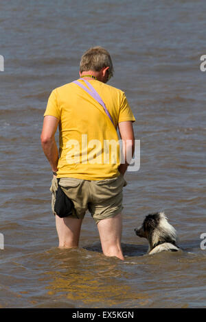 Uomo correre e giocare in mare con il suo sheepdog AUSTRALIANO KELPIE o, Crosby, Liverpool, Merseyside, Regno Unito Foto Stock