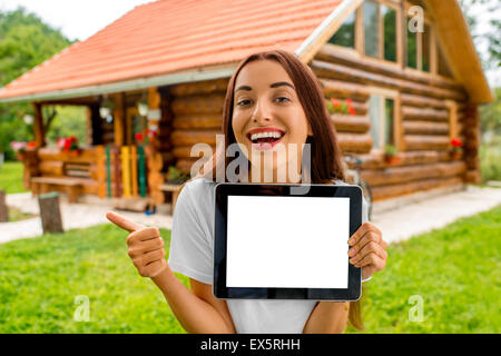 La donna che mostra digitale compressa vicino al cottage di legno. Foto Stock