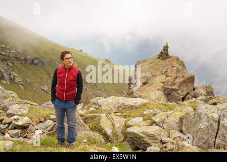 Escursionista femmina di raggiungere il suo obiettivo alla cima della montagna e guardando al di sopra in una torbida e nebbioso giorno. Avventure estive nelle Alpi. Foto Stock