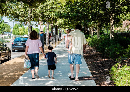 Due genitori camminare lungo un marciapiede con i loro due bambini piccoli, un ragazzo e una ragazza. Foto Stock