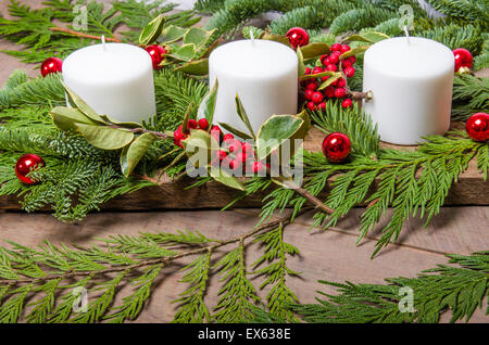 Un sempreverde Natale centrotavola con tre candele bianche su base di legno Foto Stock