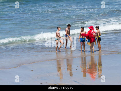 Croce Rossa (Cruz Roja) femmina lifeguard per spiegare i pericoli di riptides ai giovani ragazzi sulla spiaggia popolare tra i surfisti in Spagna Foto Stock