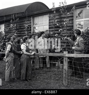 Storico degli anni cinquanta, gruppo di maschio e femmina farm o apprendisti rurali al di fuori di essere istruito dal tutor. Foto Stock