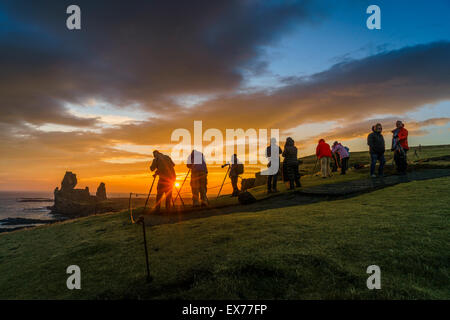 Il sole di mezzanotte e fotografi dal mare Londrangar pile e le scogliere Thufubjarg. Snaefellsnes Peninsula, Islanda Foto Stock