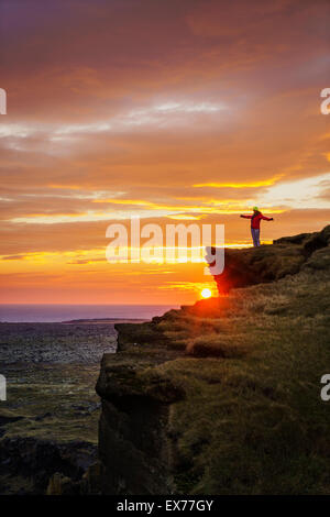 Persona sulle scogliere con il sole di mezzanotte e, Londrangar pile di mare e le scogliere Thufubjarg. Snaefellsnes Peninsula, Islanda Foto Stock