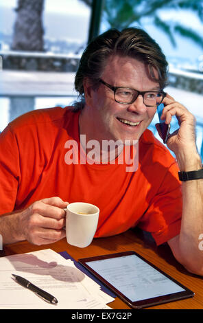 Tecnologia intelligente business all'estero vacanza uomo sorridente maturo utilizzando iPhone smartphone e iPad air tablet computer in villa di lusso hotel piscina al crepuscolo Foto Stock