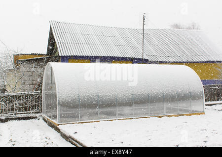 La serra di plastica si trova sulla terra e coperto dalla caduta di neve Foto Stock
