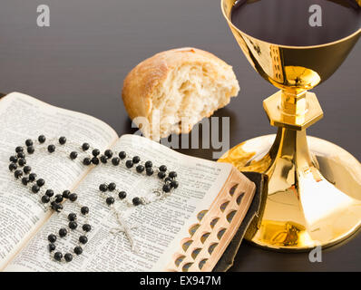 La Santa Bibbia con il nero del rosario, il pane e il calice in oro con il vino Foto Stock