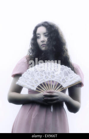 Una bella donna con lunghi capelli ricci in un abito rosa con un ventilatore bianco Foto Stock