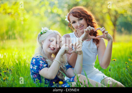 Ritratto di felice madre e figlia giovane con il cuore in una splendida fioritura di frutta giardino con fiori bianchi su alberi di mele Foto Stock